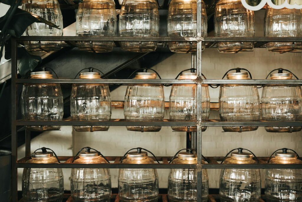 Rows of empty glass jars on metal shelves in a dimly lit environment.