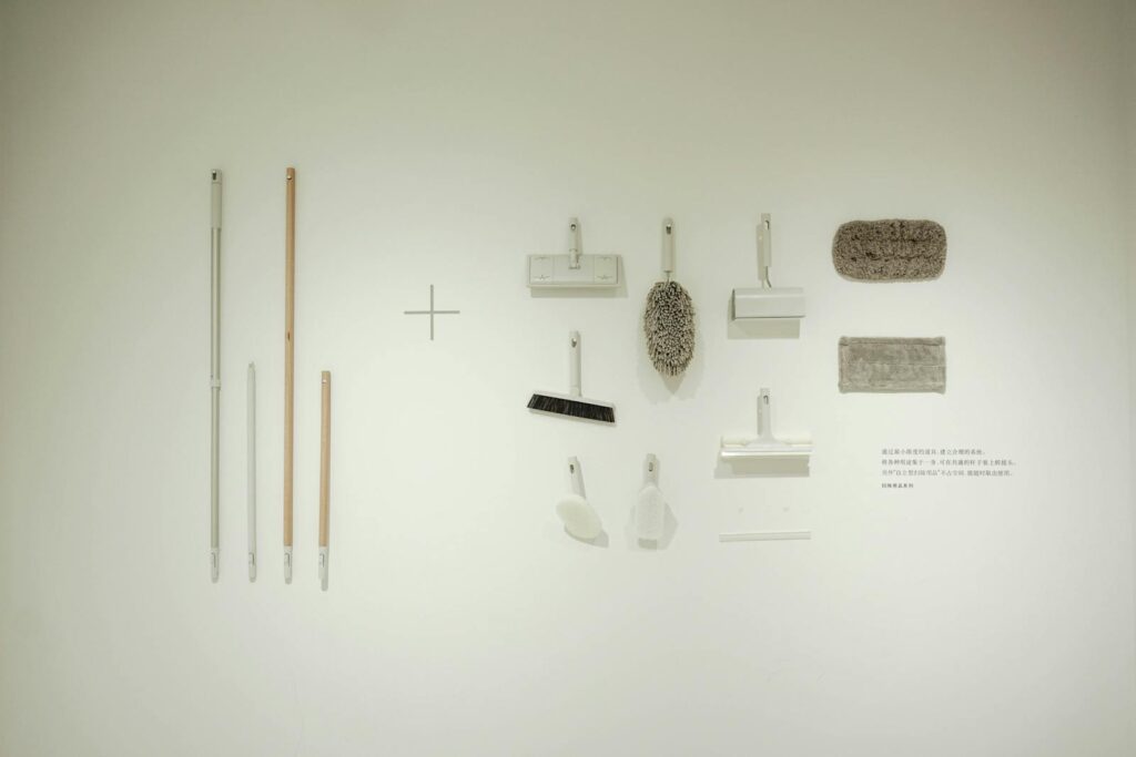 A minimalist flat lay of various cleaning tools arranged on a white wall, showcasing a modern concept.