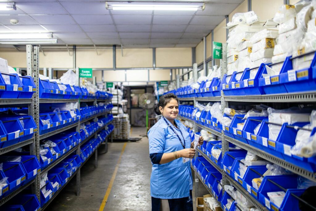 Female worker organizing inventory in a warehouse with blue bins and bright lighting.