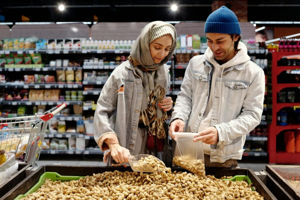 A man and woman select peanuts in a grocery store aisle during a shopping trip.