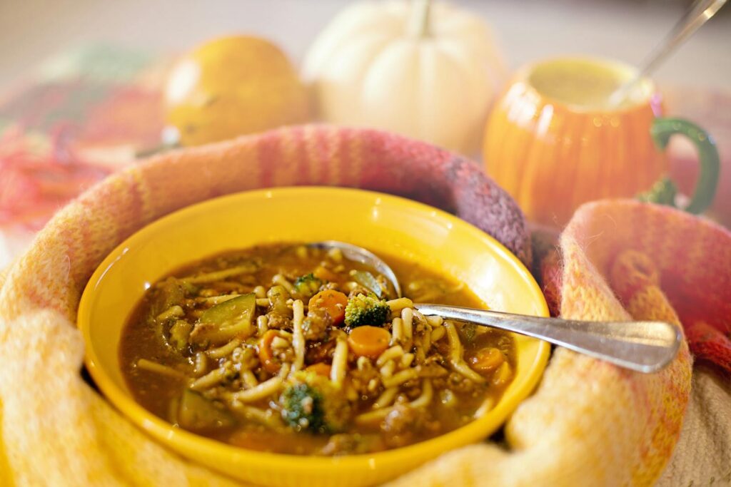 A comforting bowl of vegetable noodle soup surrounded by cozy autumn decor, perfect for a warm and hearty meal.