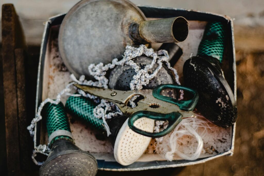A collection of rustic gardening tools including scissors, watering can tips, and threads in a vintage box.