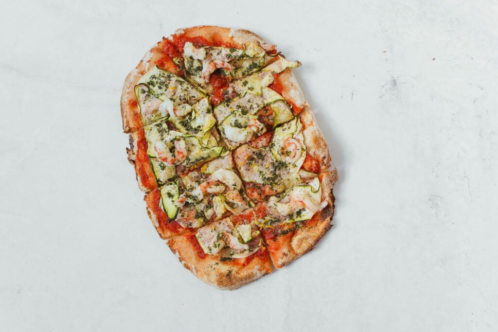 Sliced Italian flatbread pizza topped with cheese, zucchini, and herbs on a white background.