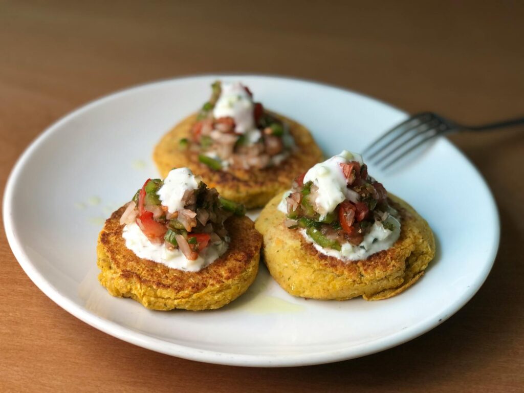 Mouth-watering zucchini fritters topped with fresh salsa and yogurt on a ceramic plate.