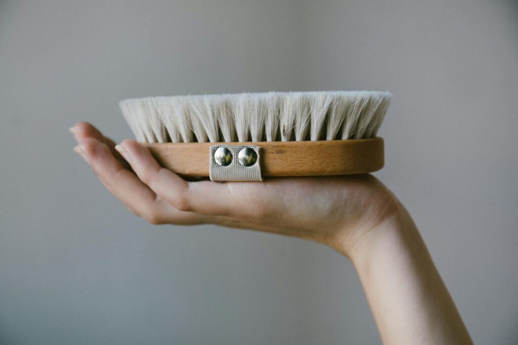 A detailed shot of a hand gracefully holding a natural bristle wooden brush with a strap.