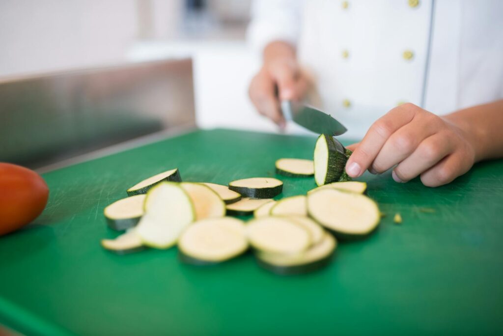 Close-up of a chef slicing zucchini on a green chopping board for fresh cooking.