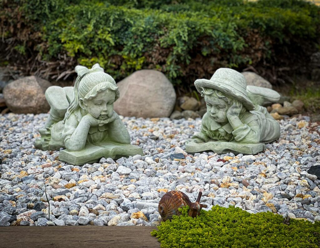 Whimsical sculptures of children reading amidst a tranquil garden setting.