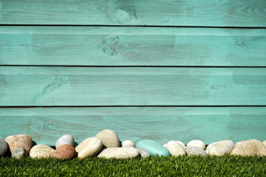 Turquoise wooden planks with pebbles and grass, perfect for a serene background.