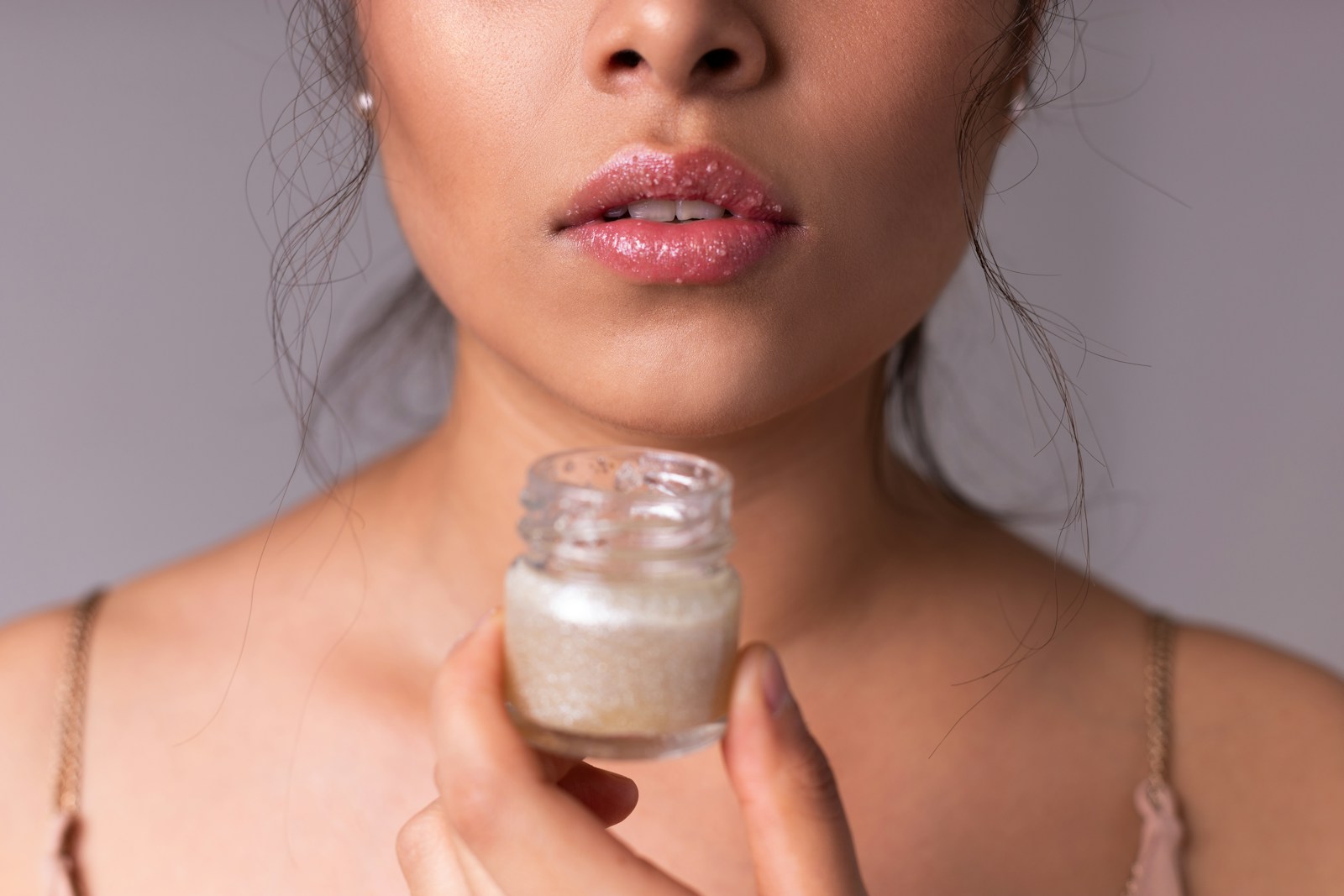 Woman holding white plastic bottle of lip balm.