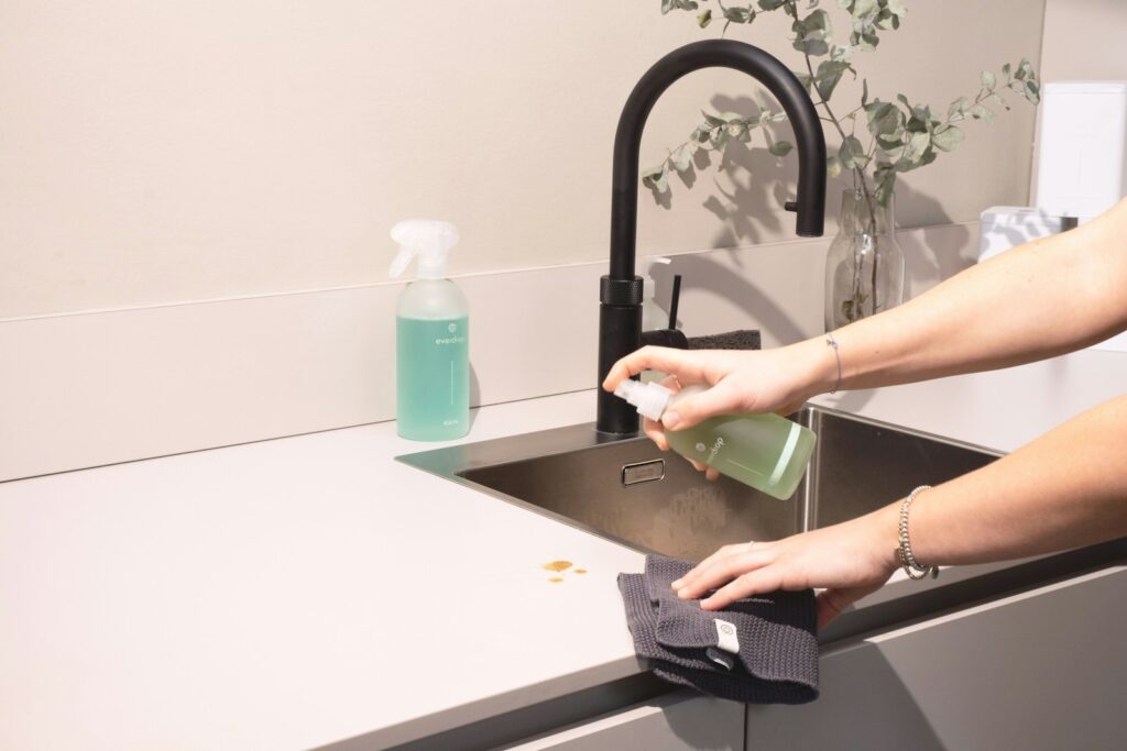 A woman is cleaning a kitchen sink with a rag