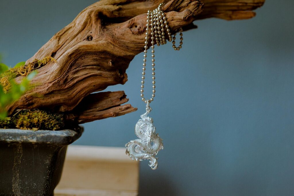 Close-up of a vintage silver dragon pendant elegantly hanging on a textured driftwood piece.