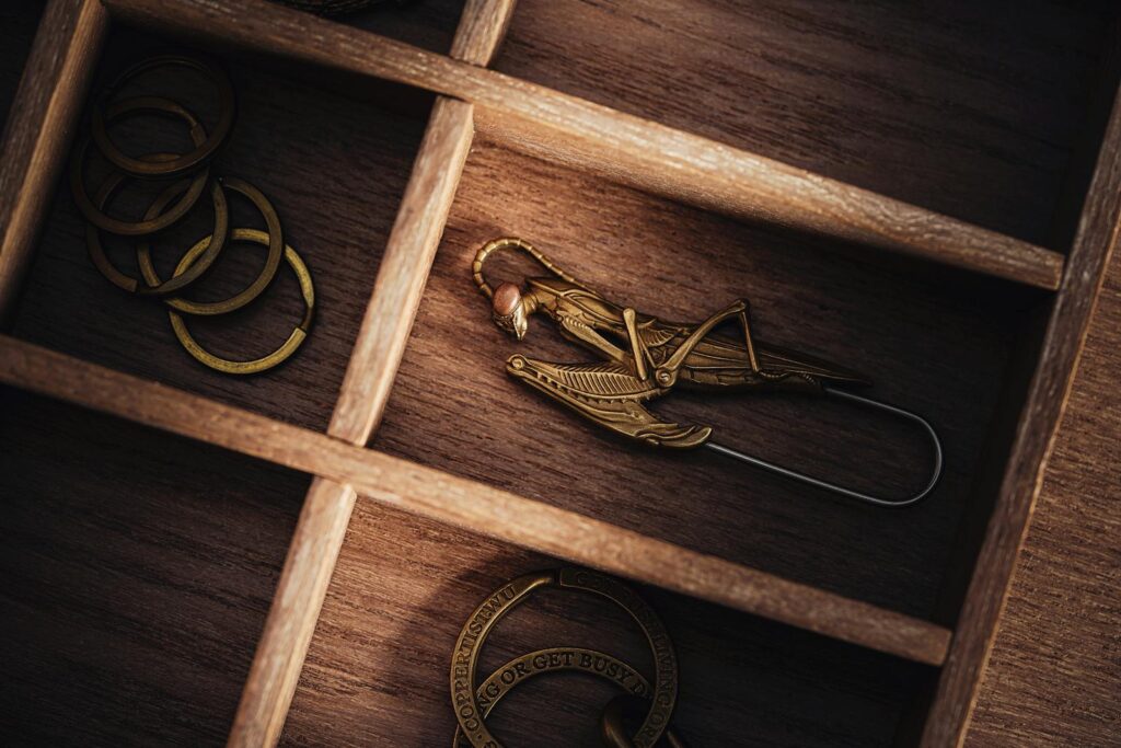 Intricate metal brooch shaped like an insect displayed in a wooden drawer.