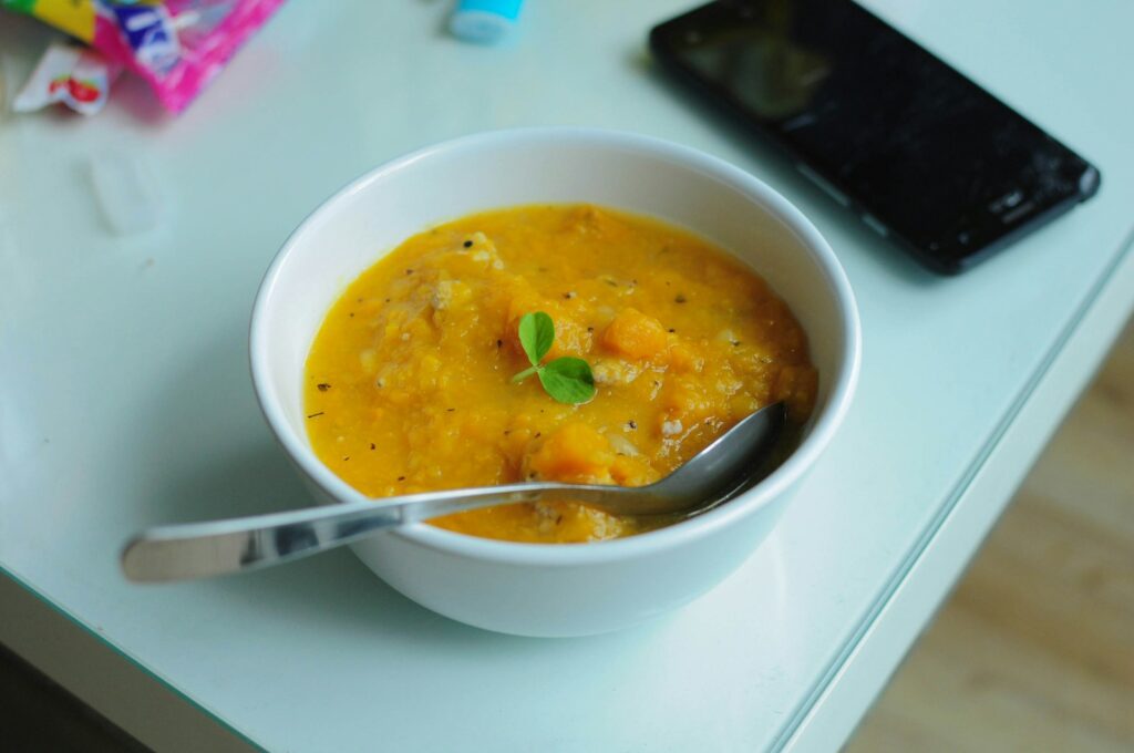 Bowl of soup with spoon beside smartphone