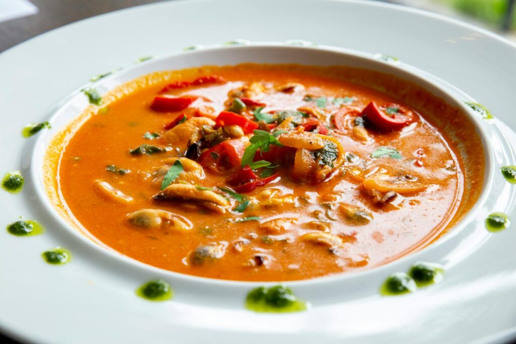 Hearty tomato seafood soup garnished with fresh herbs and peppers, bursting with flavor.