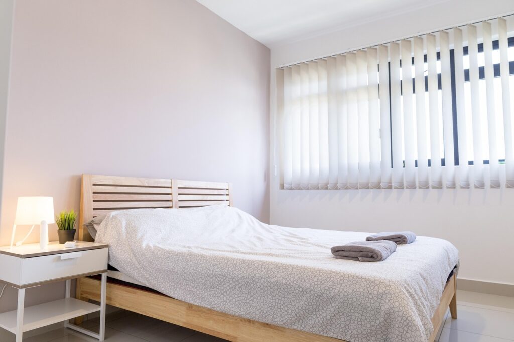 A serene bedroom scene showcasing a comfortable bed, white walls, and a window allowing soft light to enter.