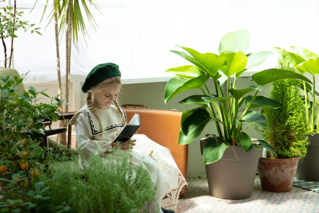 A young girl enjoying a book surrounded by lush indoor plants in a sunny room.
