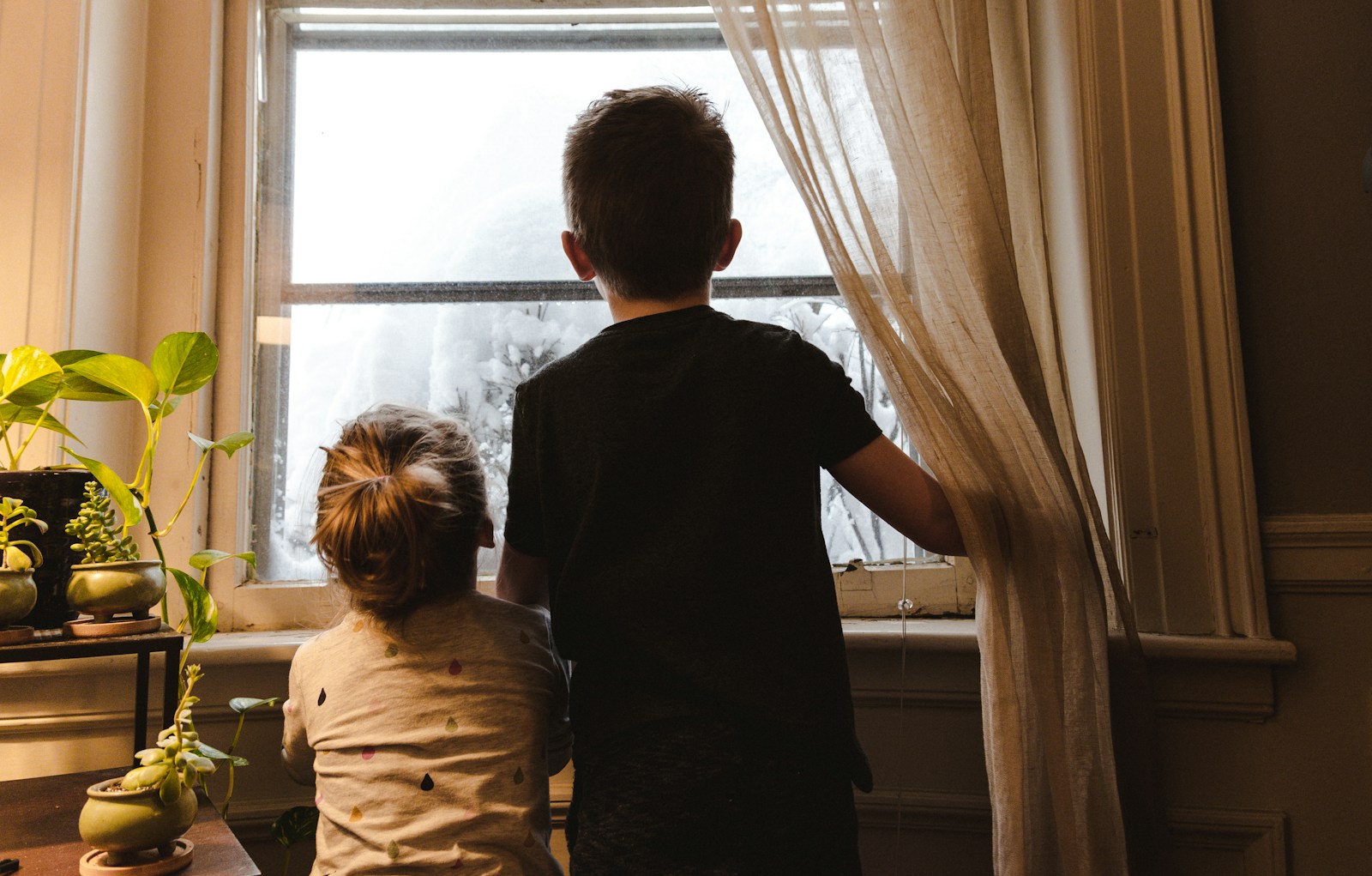 Boy and girl standing near window looking outside