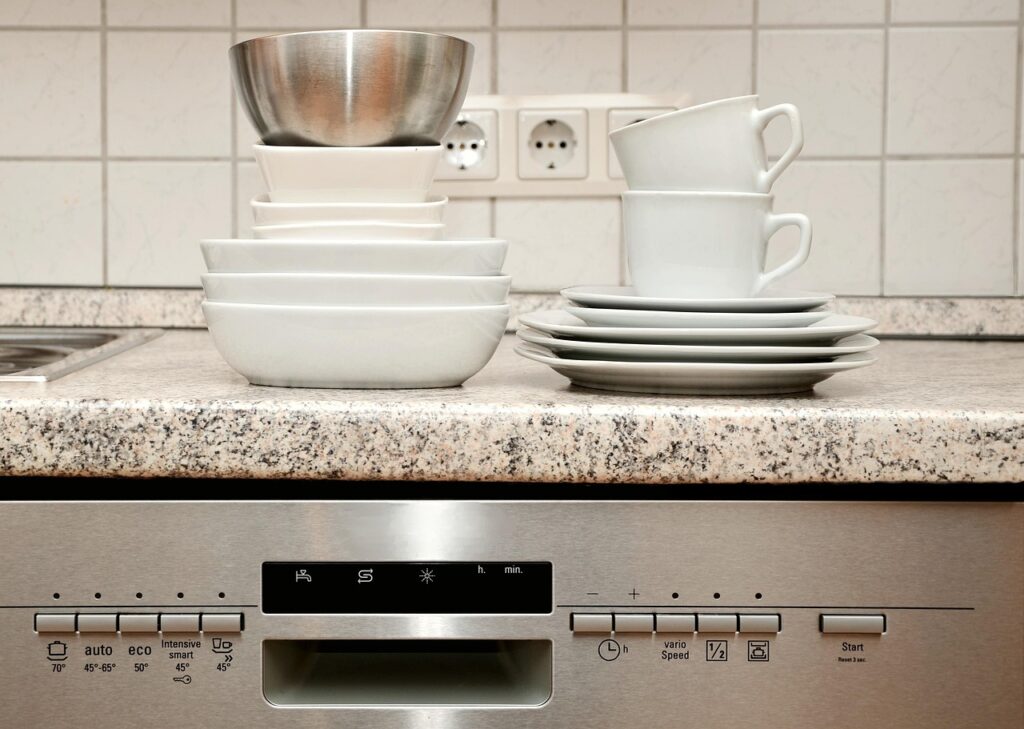 A pile of clean dishes and cups placed on a dishwasher, showcasing organized kitchenware before loading.