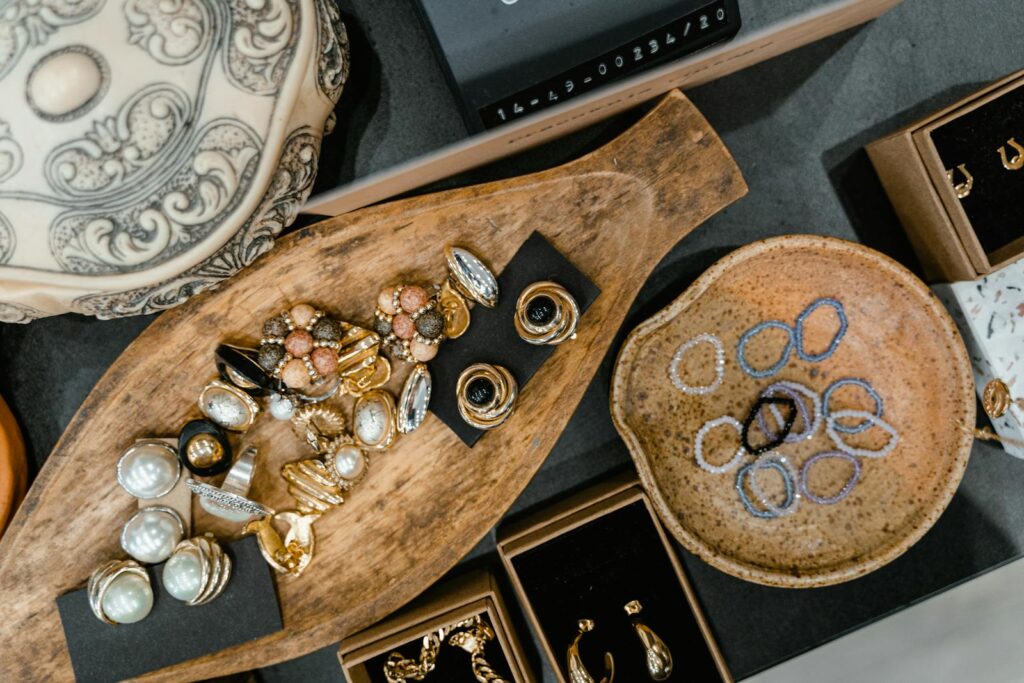 A top view of assorted jewelry including rings and bracelets in a wooden tray and ceramic dish.