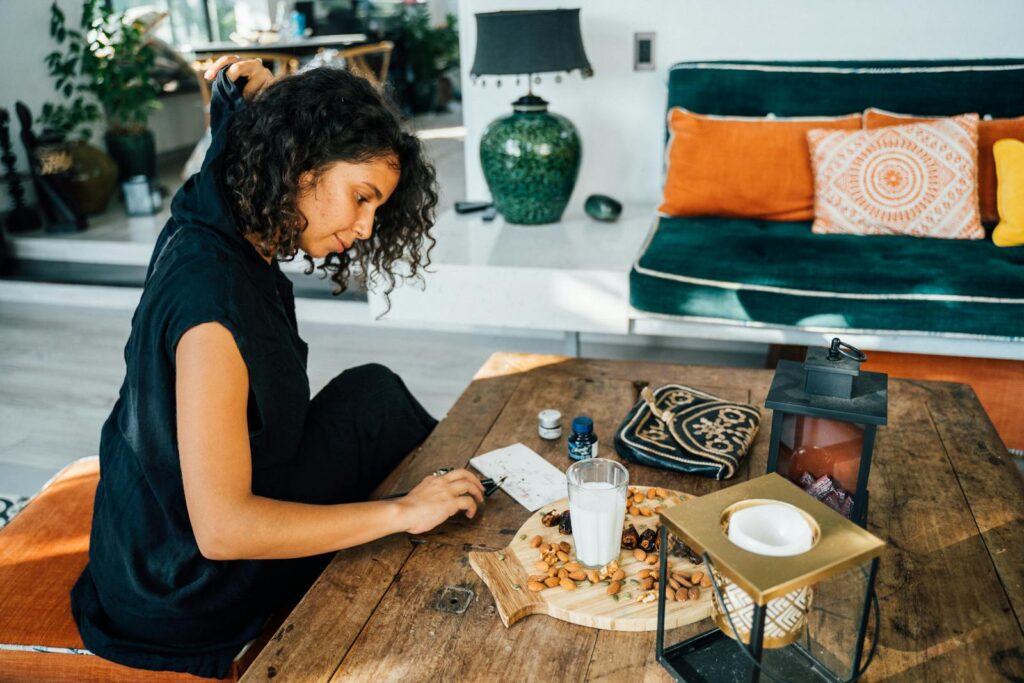 Curly-haired woman indoors sitting at a table with milk, nuts, and decorative items.