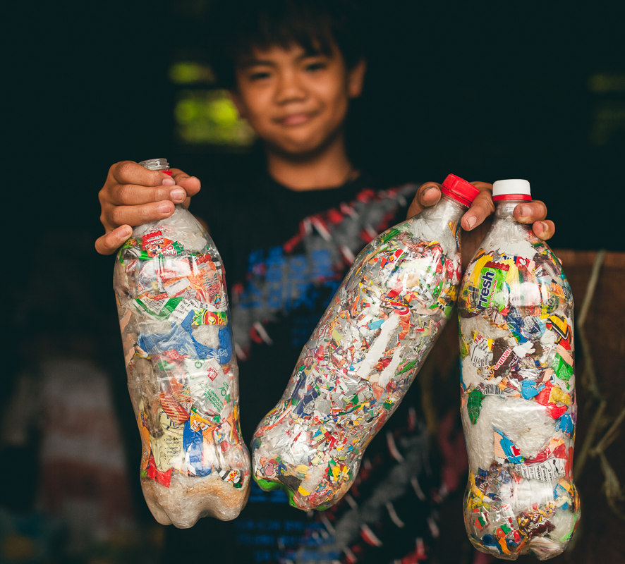 A young boy holds up three plastic bottles, smiling as he promotes recycling and environmental responsibility.