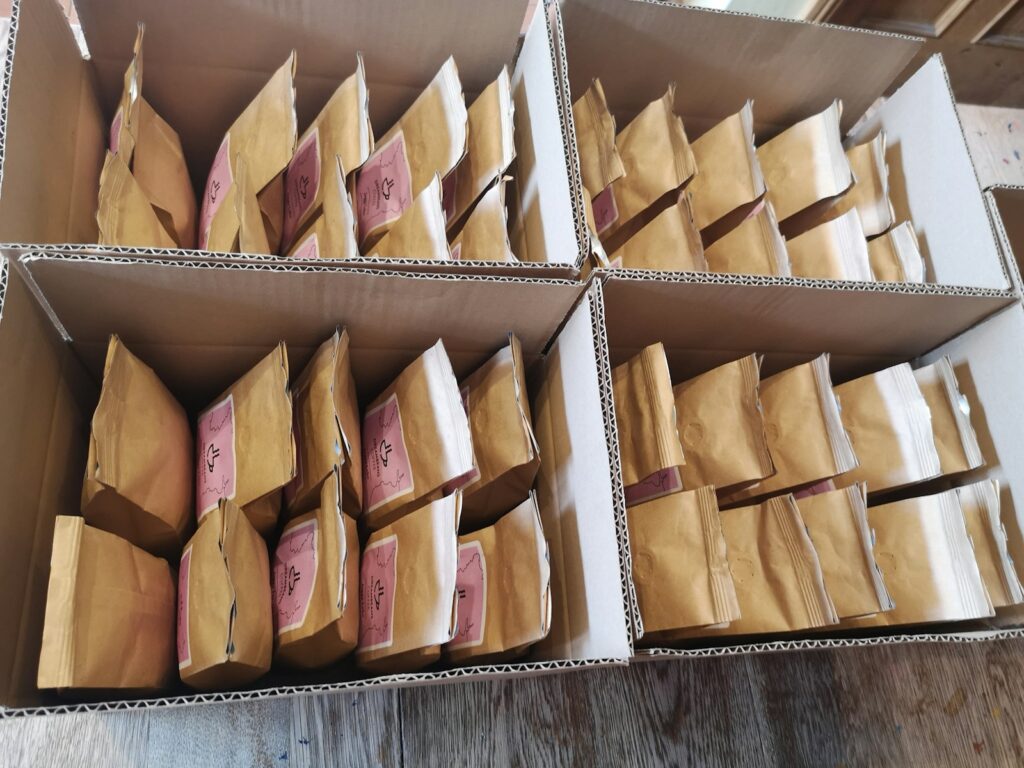 A box containing brown paper bags alongside pink and white decorative paper, ideal for unique gift packaging.