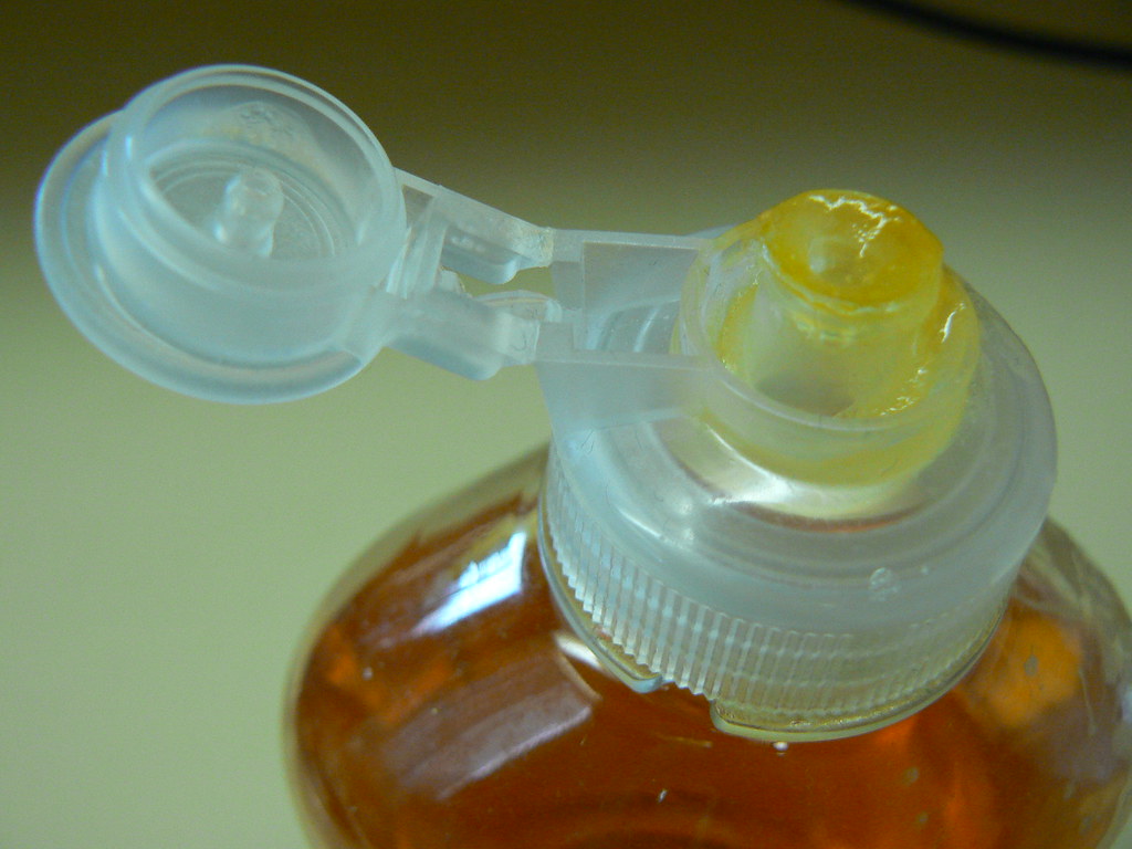 A bottle containing a bright orange liquid, positioned upright, with sunlight highlighting its vivid hue and smooth surface.