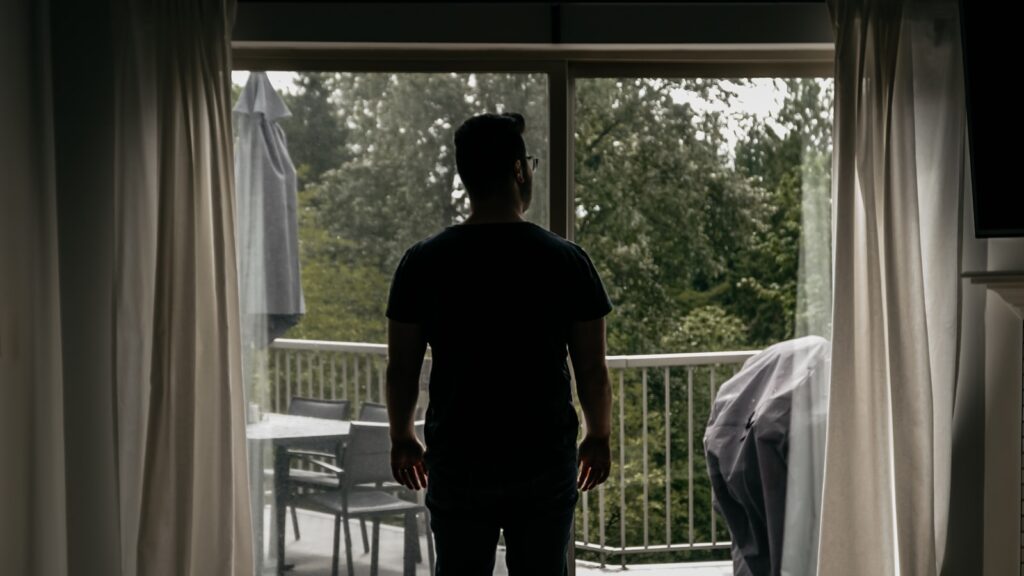 Man in black crew neck t-shirt standing near white window.