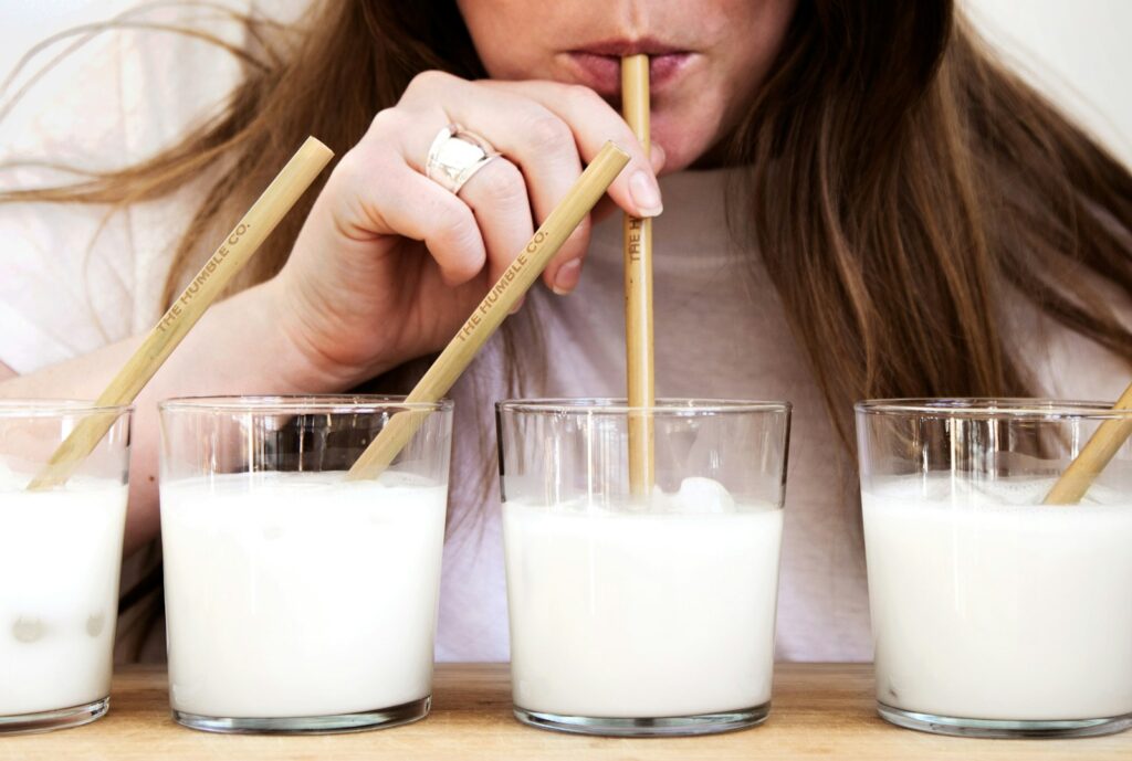 Woman holding brown wooden straws sippiing milk.