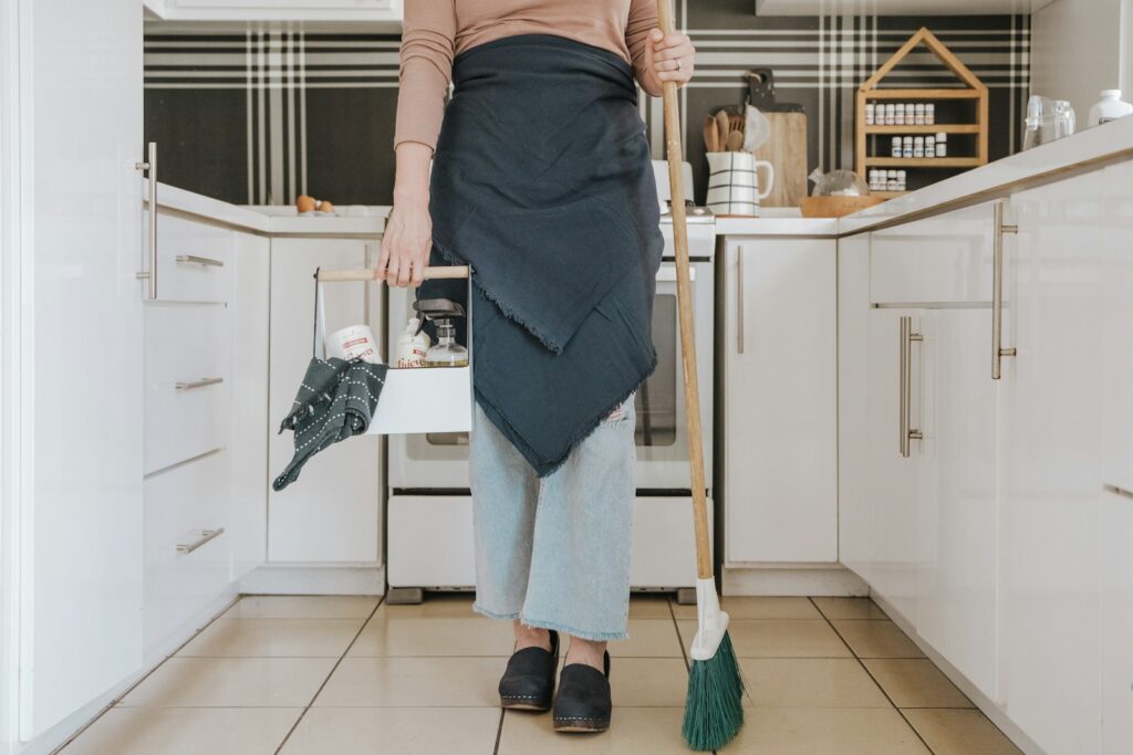 A woman standing in a kitchen holding a broom