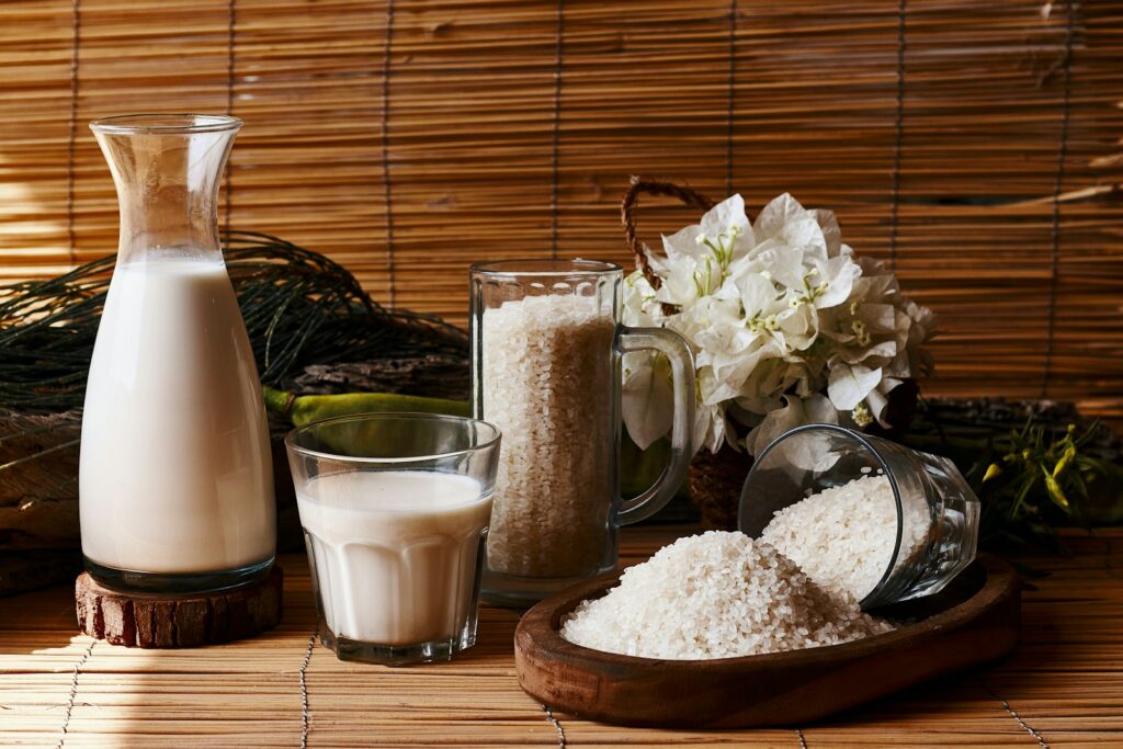 A table topped with a pitcher of milk next to a glass of rice milk.