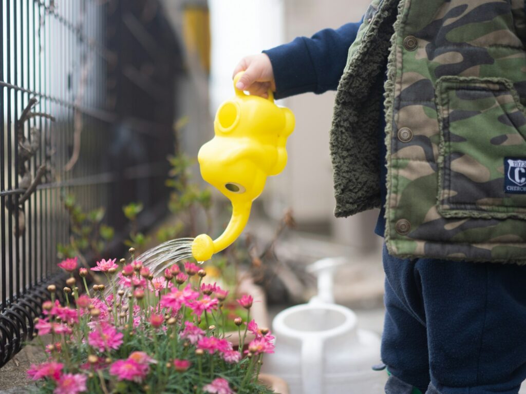 A child joyfully waters colorful flowers using a bright yellow watering can in a sunny garden.