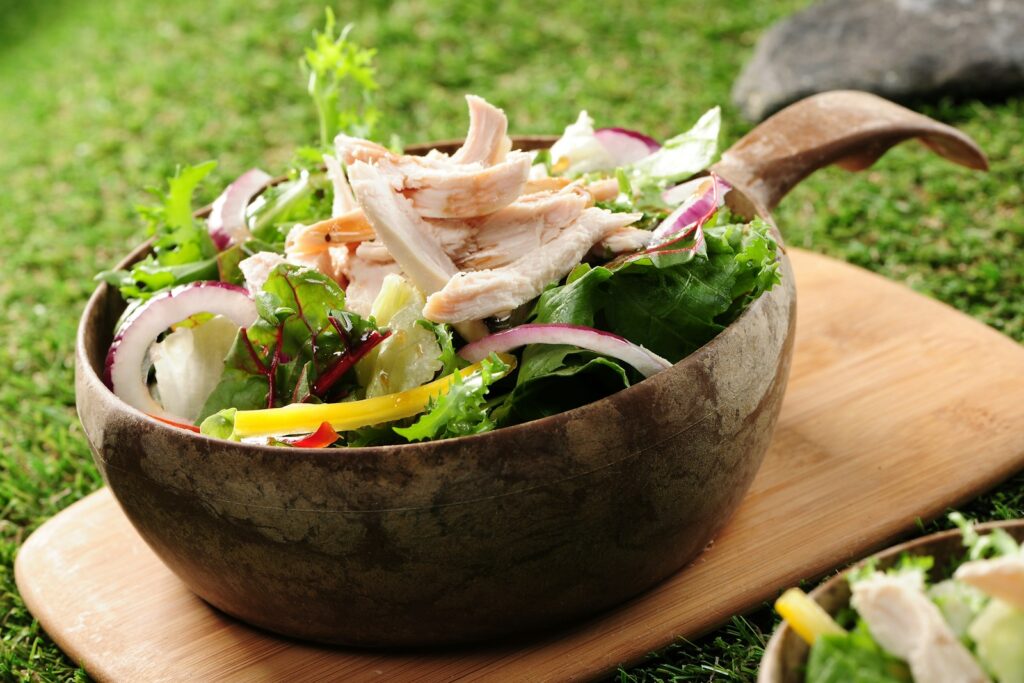 A wooden bowl filled with a salad on top of a wooden board