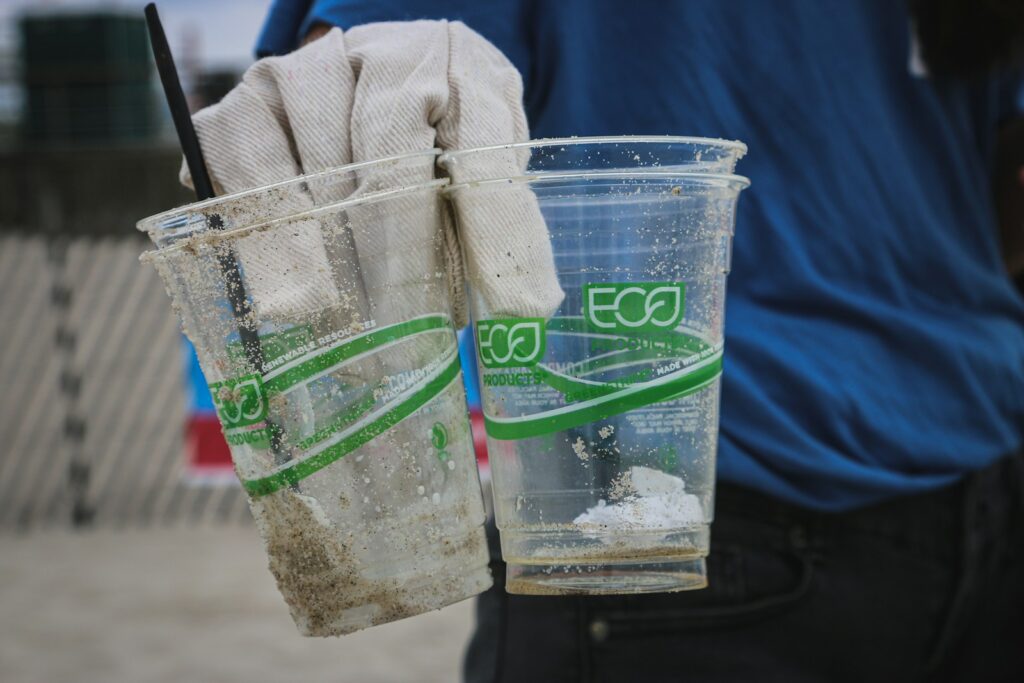 Person holding two clear plastic disposable cups.