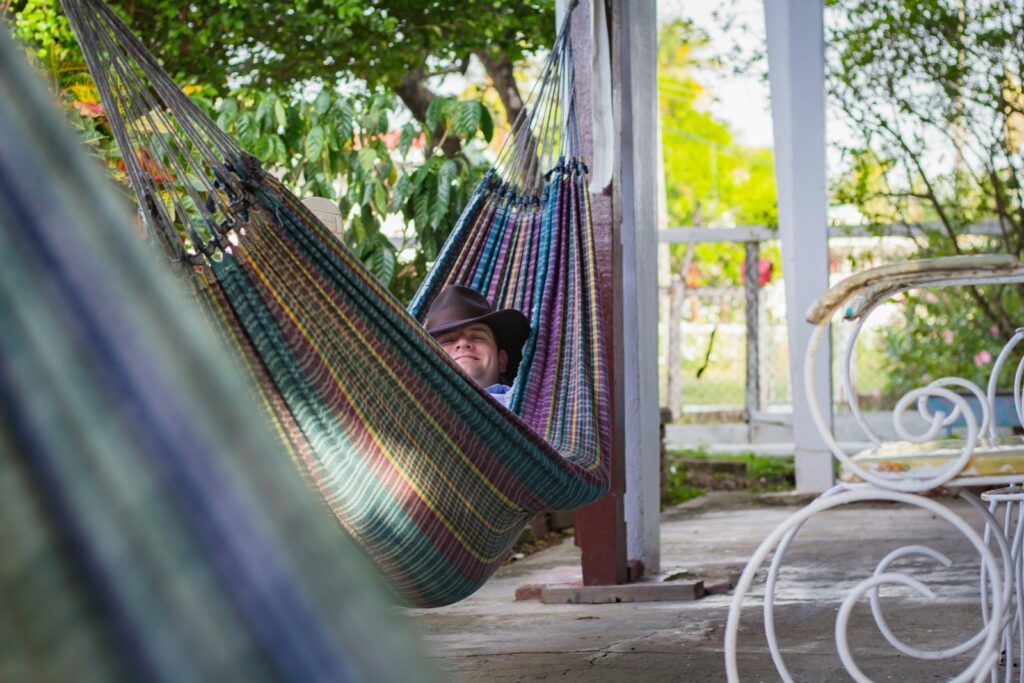 Man laying down on multicolored hammock hanged on porch column.